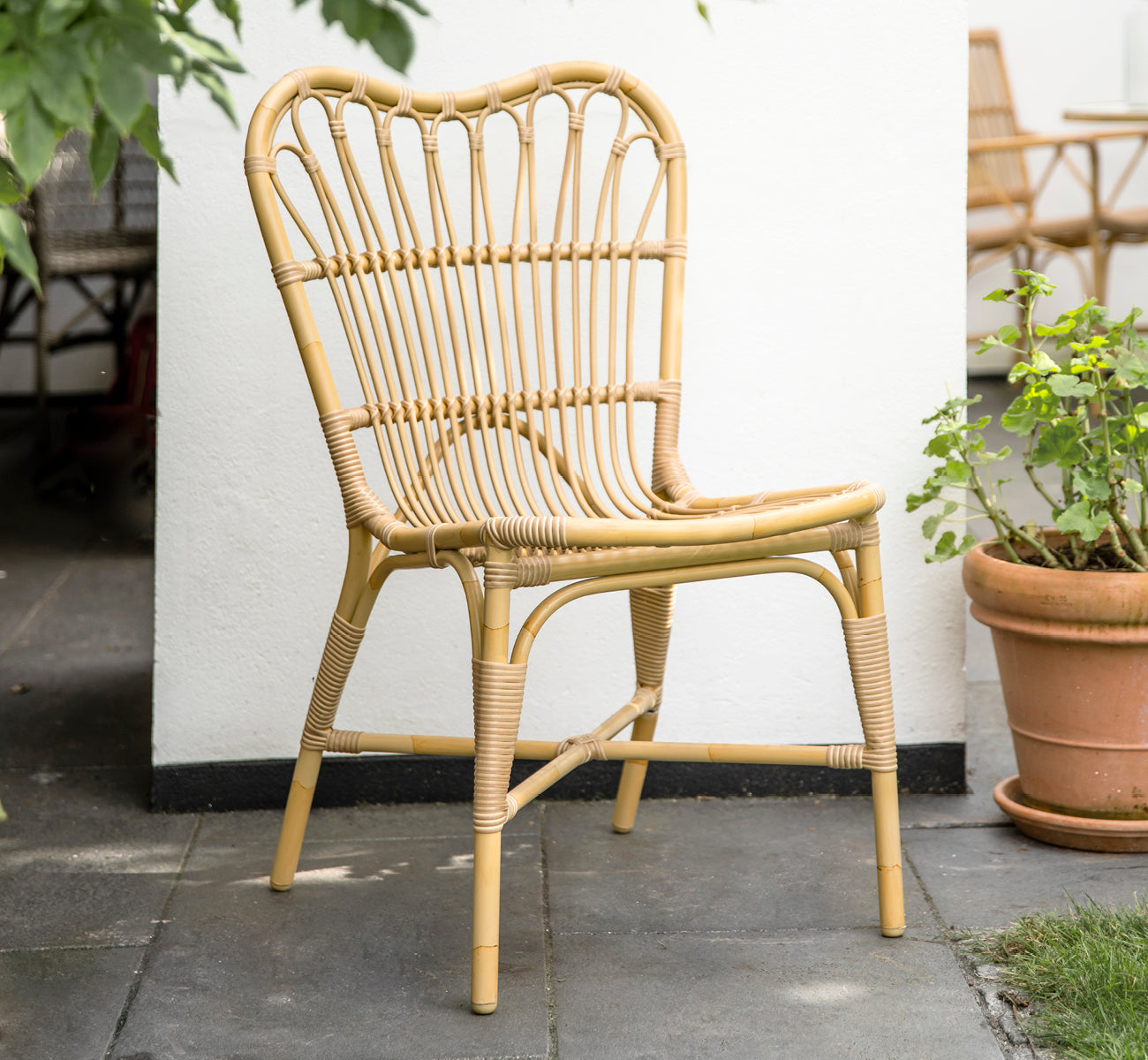 Dette er et livsstilsbillede af Margret Udendørs spisebordsstol i natural aluminium artfibre. Hvid gårdhave med terrakottakrukker og planter.