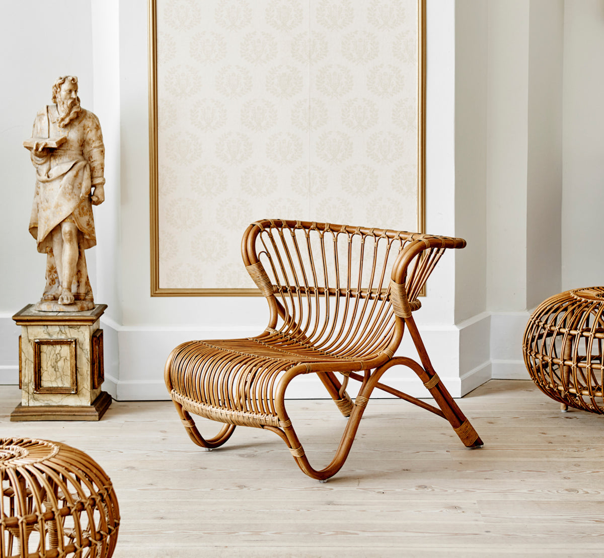 Dette er et livsstilsbillede af Fox Lænestol i polished Antique Rattan, i et varmt interiør med okkerfarvet lambrisering og mørkt sildebensgulv.