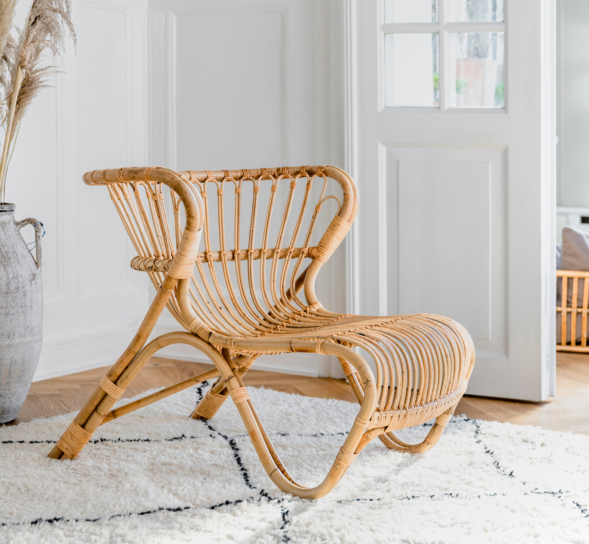 Dette er et livsstilsbillede af Fox Lænestol i polished Natural Rattan, i et varmt interiør med okkerfarvet lambrisering og mørkt sildebensgulv.