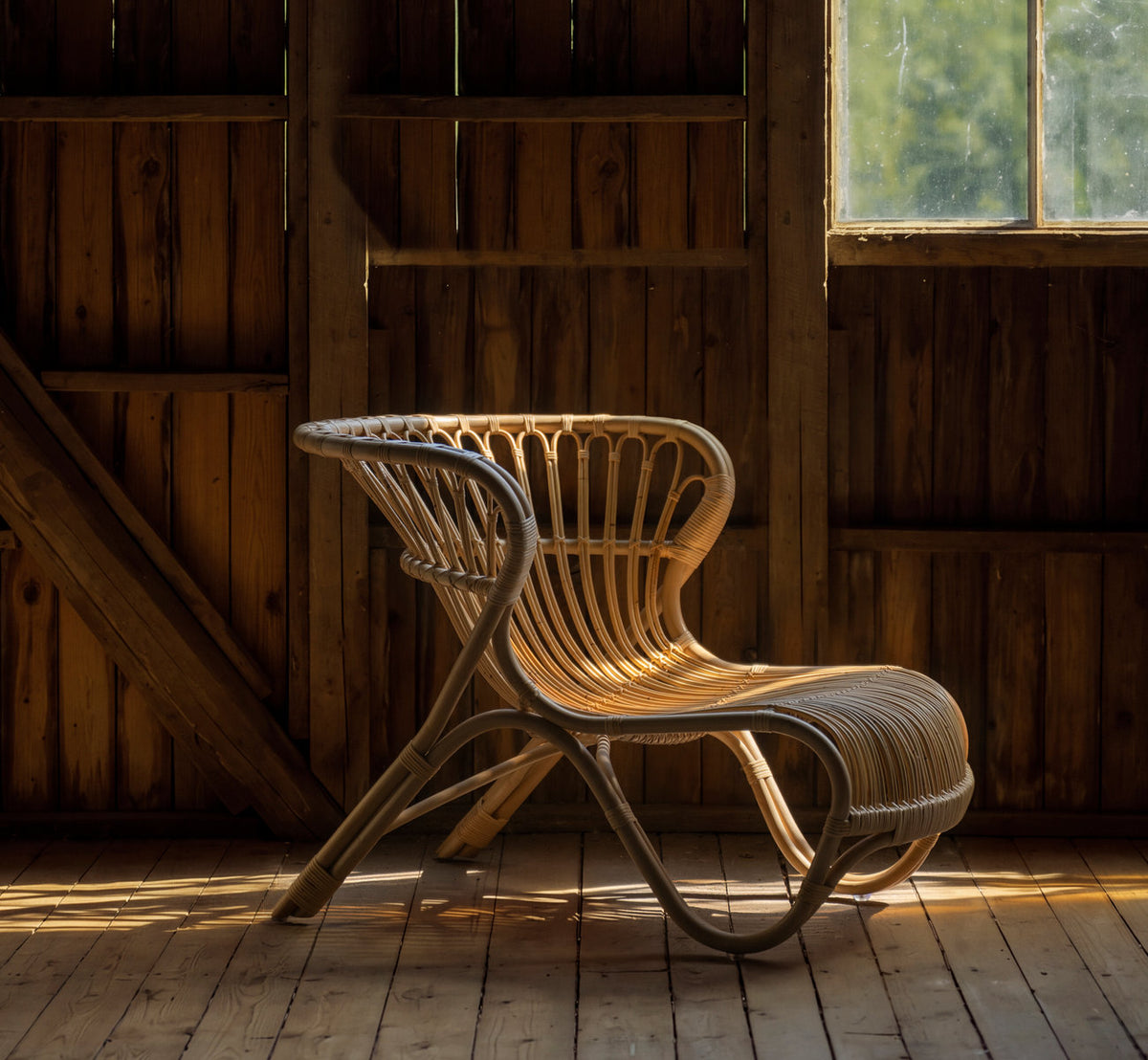 Dette er et livsstilsbillede af Fox Lænestol i polished natural rattan. I en træklædt lade med varmt lys fra vinduet.