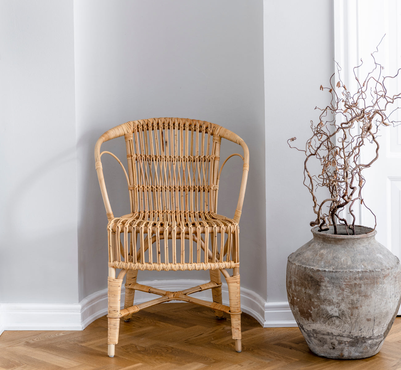 Dette er et livsstilsbillede af Robert Spisebordsstol i polished natural rattan. Placeret ved siden af et søjlebord med tulipaner på et jutetæppe.