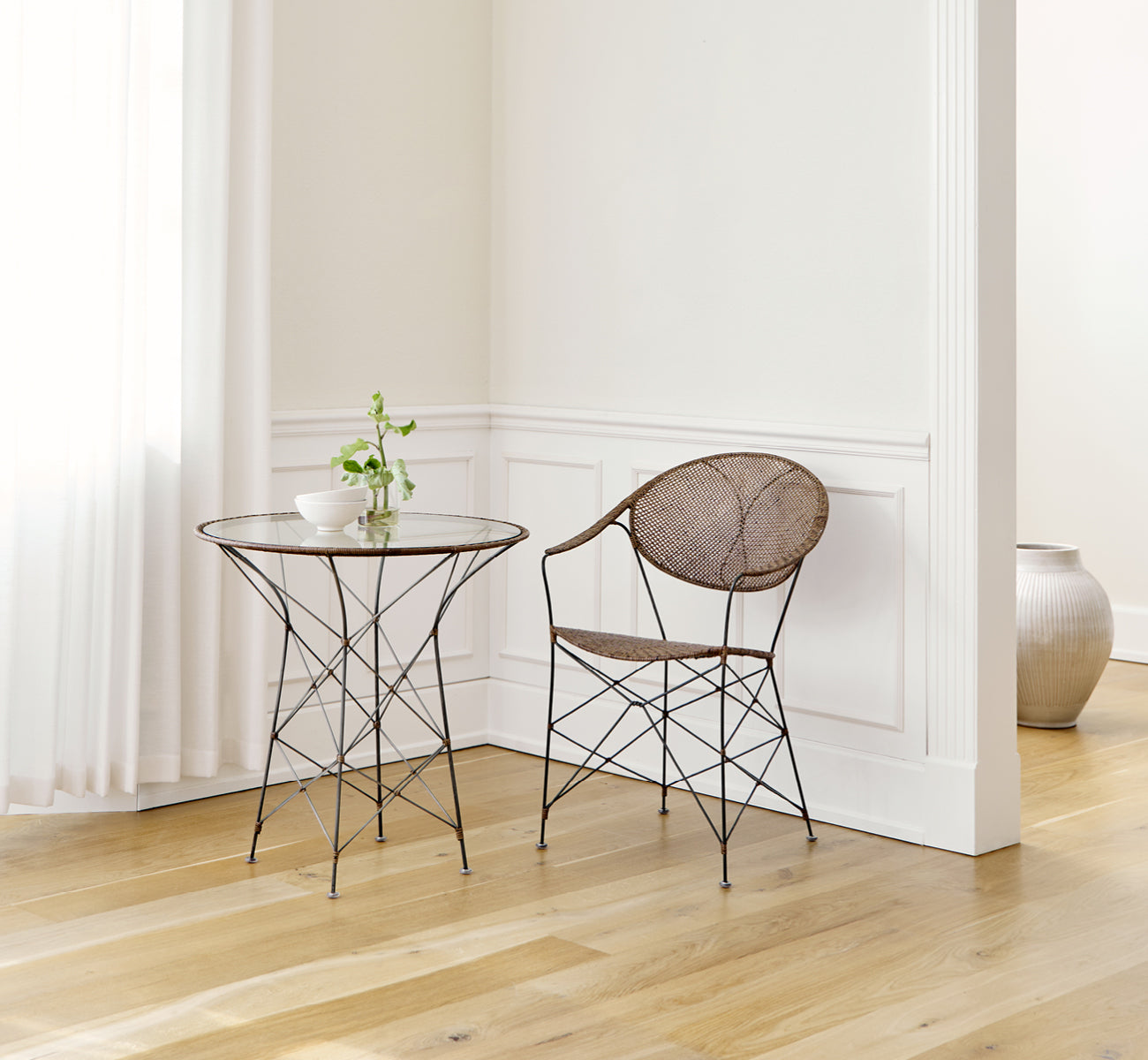 Dette er et livsstilsbillede af Funky Spisebordsstol i hazelnut rattan iron frame, i et lyst interiør med hvide panelvægge og sildebensgulv.