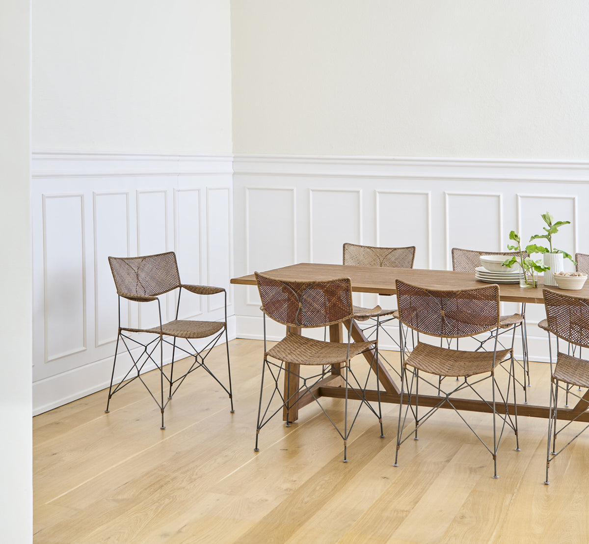 Dette er et livsstilsbillede af Rap Spisebordsstol i hazelnut rattan iron frame, i et lyst interiør med hvide panelvægge og sildebensgulv.