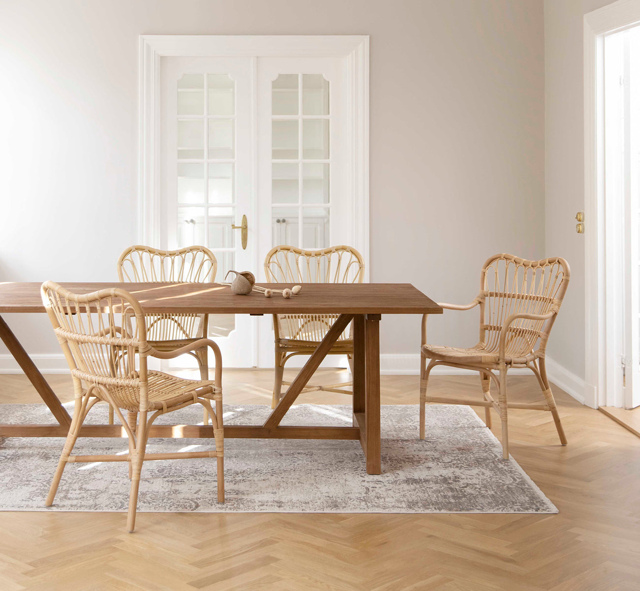 Dette er et livsstilsbillede af Lucas Teak Dining Table 240X100 cm i teak indoor. Dækket med rattanstole i et lyst rum med sildebensgulv i eg.