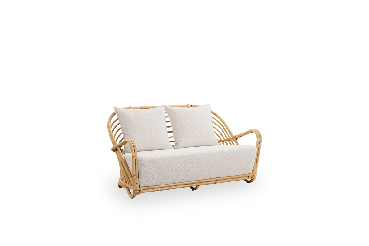 Side view af Charlottenborg 2-personers sofa i poleret naturlig rattan, designet af Arne Jacobsen. Sofaen har en buet ryg og armlæn integreret i basen, håndlavet i rattan af høj kvalitet fra Indonesien.