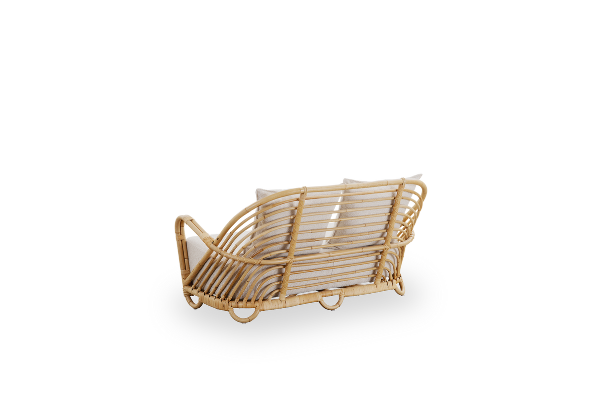 Sidevinkel bagfra af Charlottenborg 2-personers sofa i poleret naturlig rattan, designet af Arne Jacobsen. Sofaen har en buet ryg og armlæn integreret i basen, håndlavet af højkvalitets indonesisk rattan.