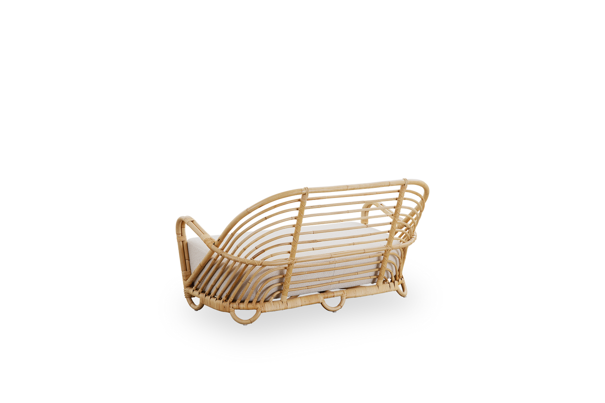 Sidevinkel bagfra af Charlottenborg 2-personers sofa i poleret naturlig rattan, designet af Arne Jacobsen. Sofaen har en buet ryg og armlæn integreret i basen, håndlavet af højkvalitets indonesisk rattan.