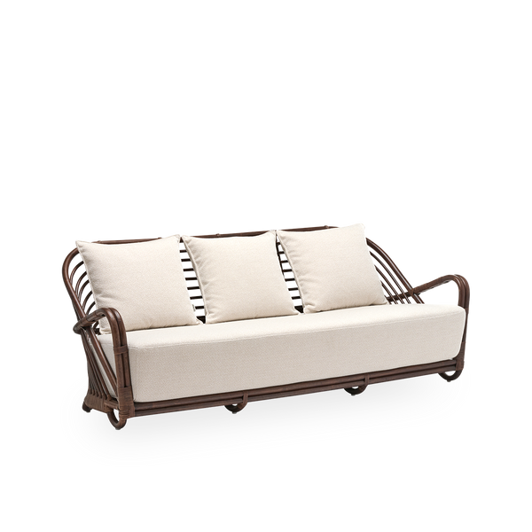 Sidevisning af Charlottenborg 3-personers sofa med sæde- og ryghynder, i brun rattan. Oprindeligt designet af Arne Jacobsen i 1936; det buede ryglæn glider elegant over i armlænene. Håndlavet i rattan.