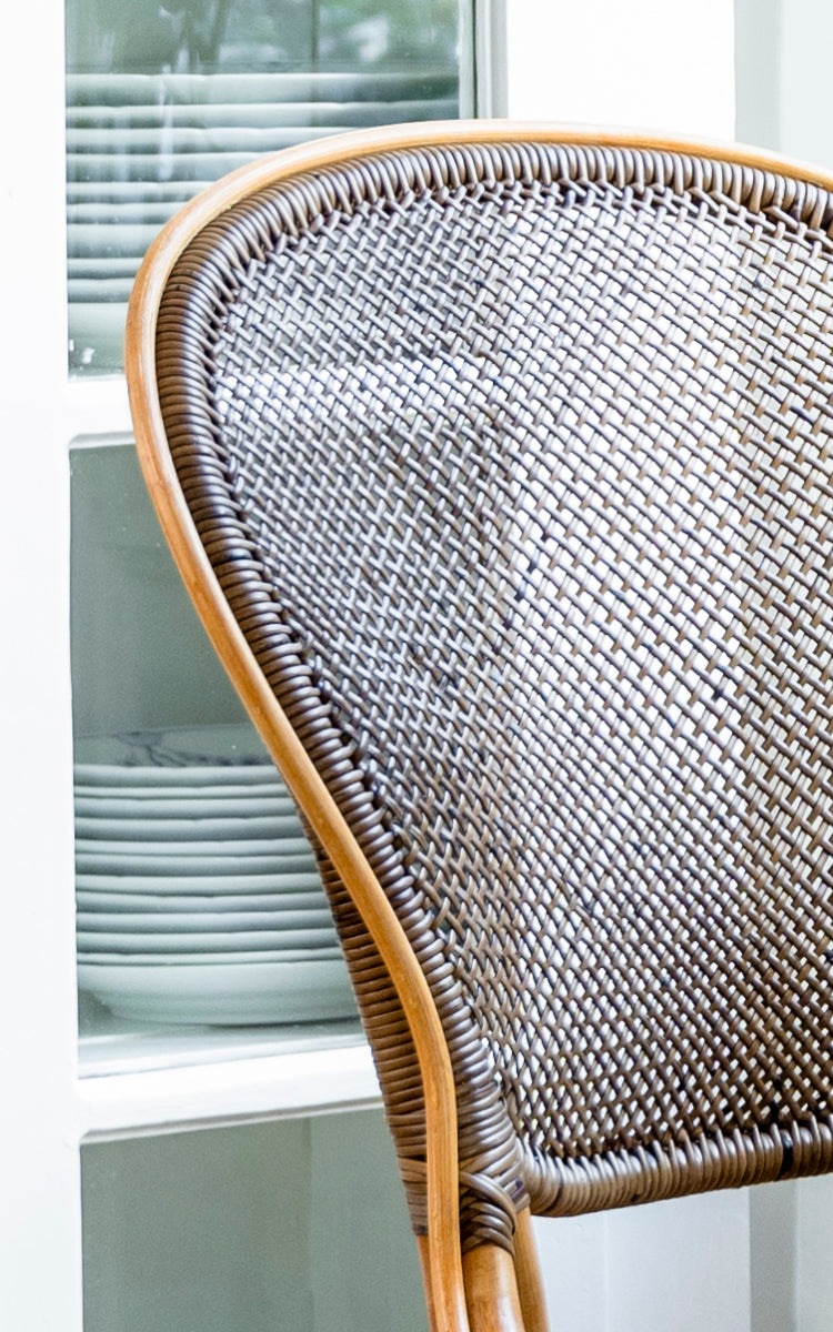 Dette er et nærbillede af Rossini Spisebordsstol i cherry rattan. Detaljeret visning af den mørke cherry rørflet-ryg mod lyse skabe.