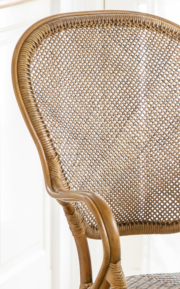 Dette er et nærbillede af Rossini Spisestuelænestol i antique rattan. Detalje af det buede rattan-armlæn, flettet sæde og omviklede samlinger.