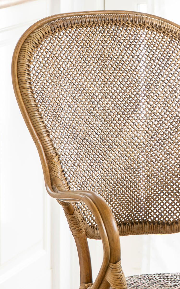Dette er et nærbillede af Rossini Spisestuelænestol i antique rattan. Detalje af det buede rattan-armlæn, flettet sæde og omviklede samlinger.