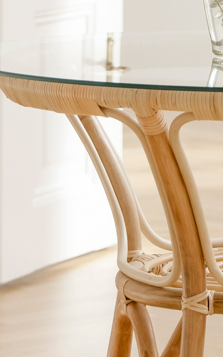 Dette er et nærbillede af Tony Café Table i natural rattan. Detalje af den runde glasplade med flettet rattan-kant og buede ben.