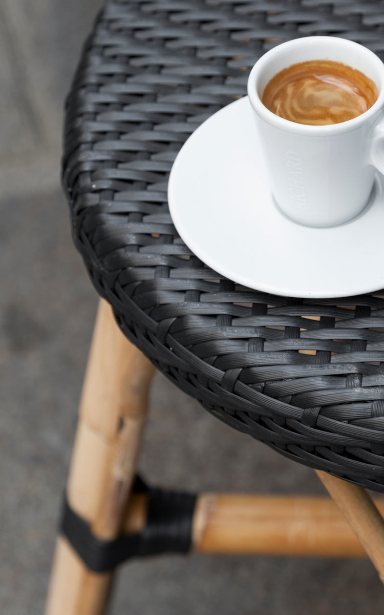 Dette er et nærbillede af Simone Skammel i black ArtFibre Skin on Rattan frame. Detalje af det flettede sæde med en espressokop ovenpå.