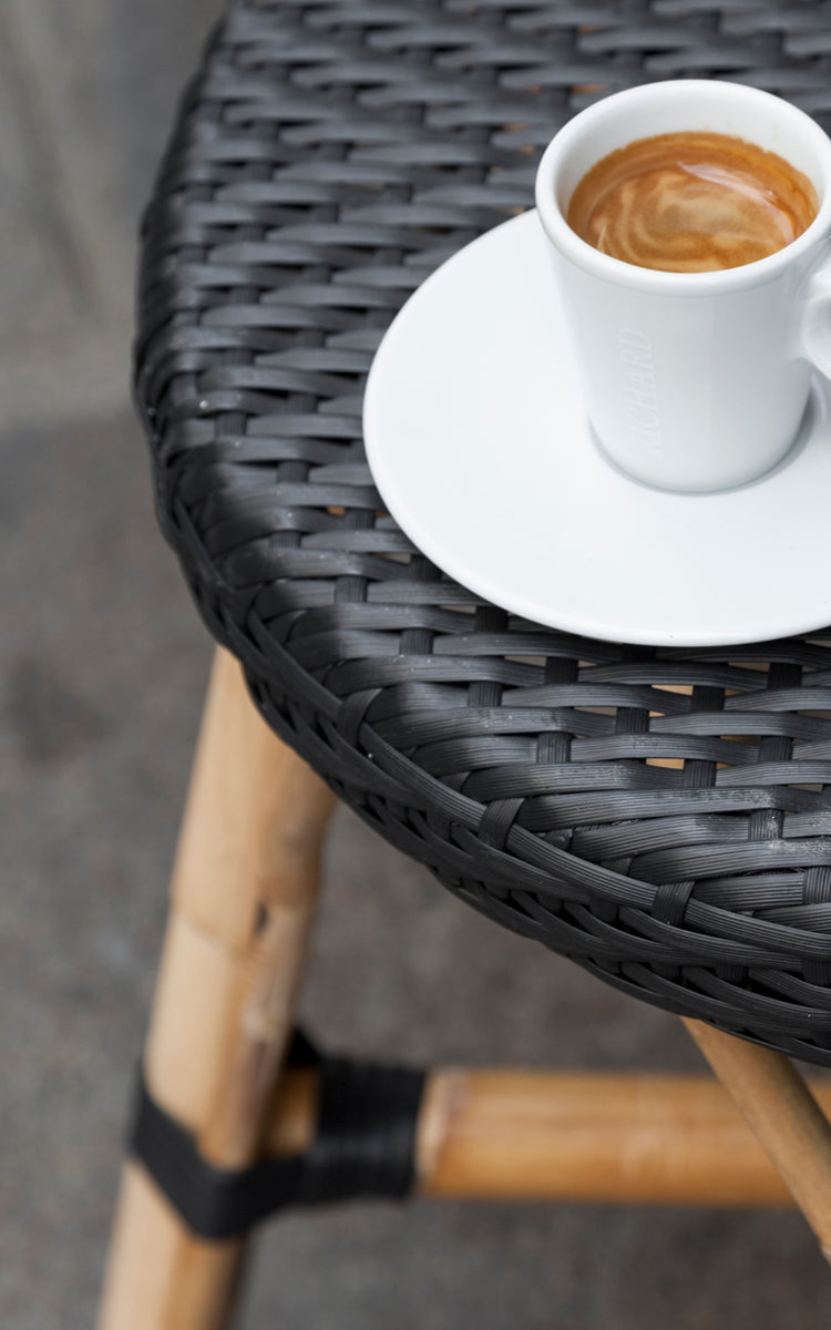 Dette er et nærbillede af Simone Skammel i black ArtFibre Skin on Rattan frame. Detalje af det flettede sæde med en espressokop ovenpå.