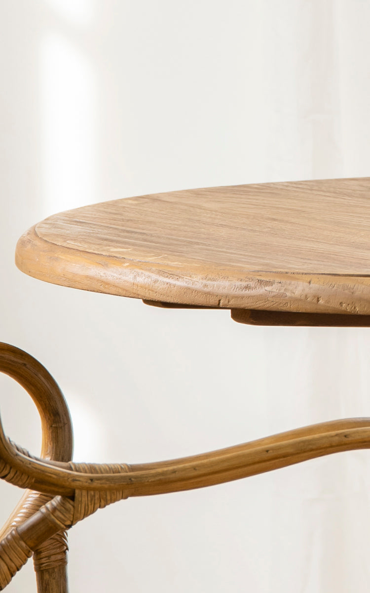 Dette er et nærbillede af Michel Teak Dining Table Ø80 cm i teak indoor. Den runde bordpladekant og den buede rattansøjlefod er vist.