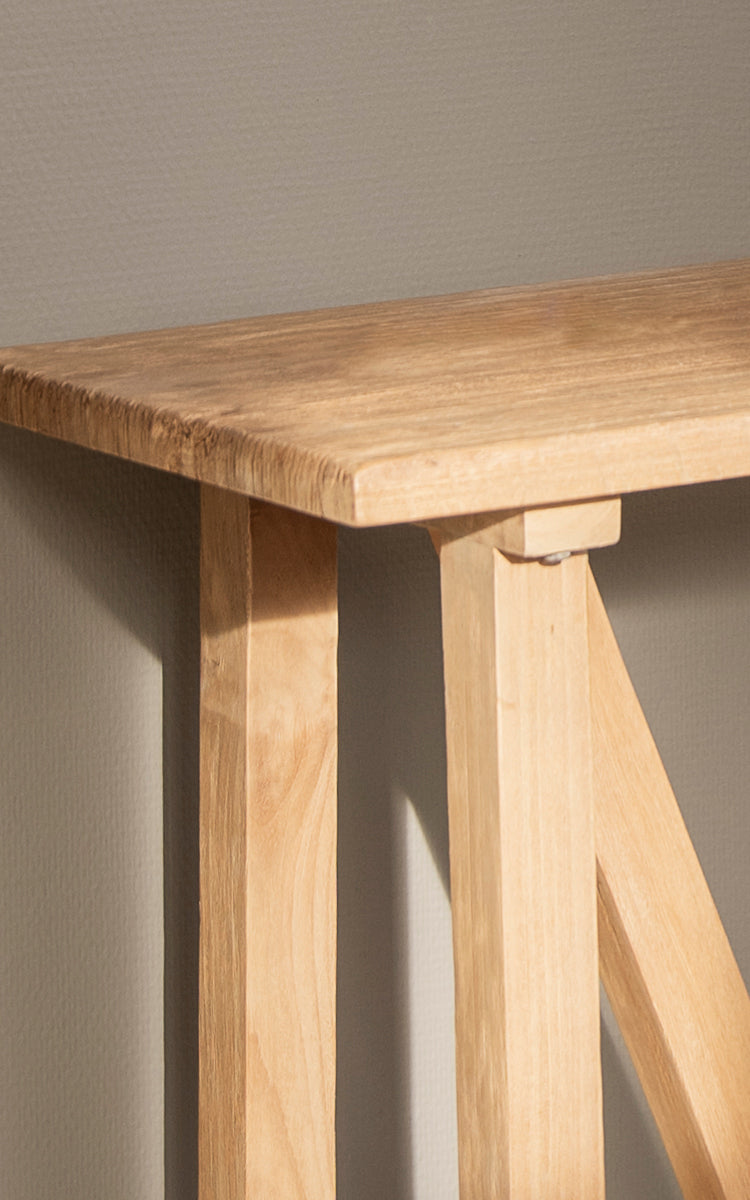 Dette er et nærbillede af Lucas Teak Konsol i teak indoor. Den solide teakoverflade og de vinklede bukkebensstel viser rene linjer og trætoner.