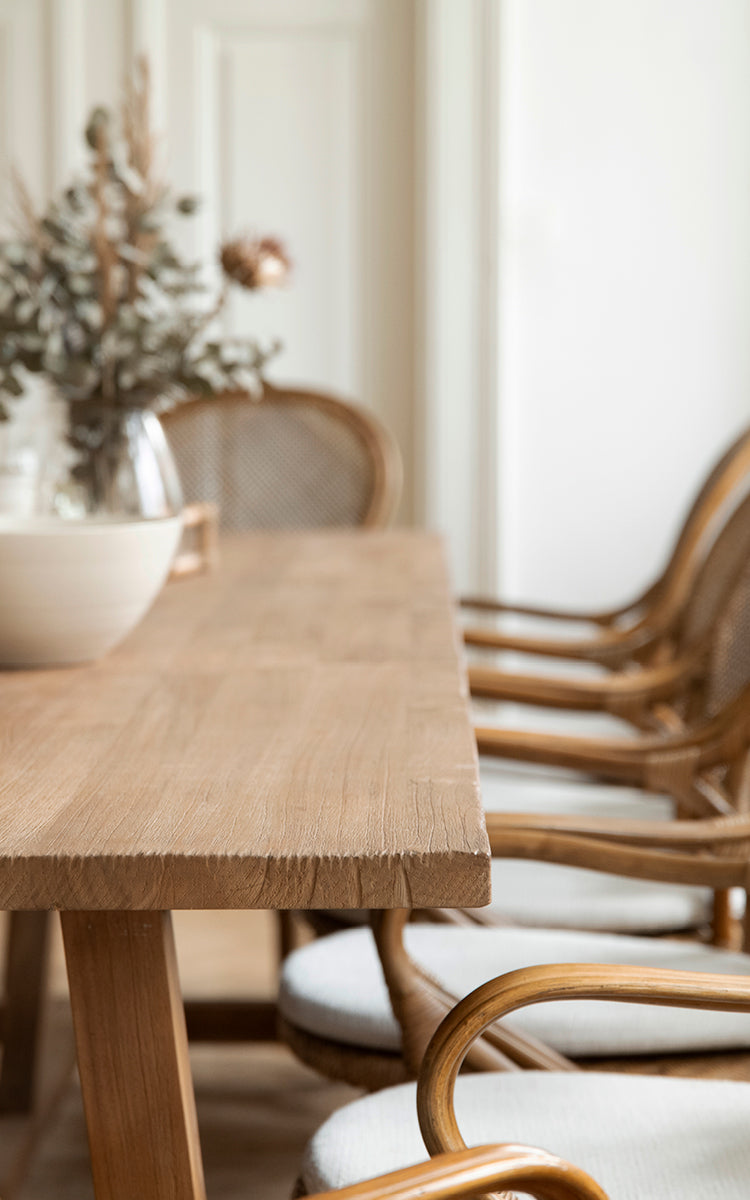 Dette er et nærbillede af Lucas Teak Dining Table 300X100 cm i teak indoor. Den solide teakkant er vist med rattanstole i baggrunden.