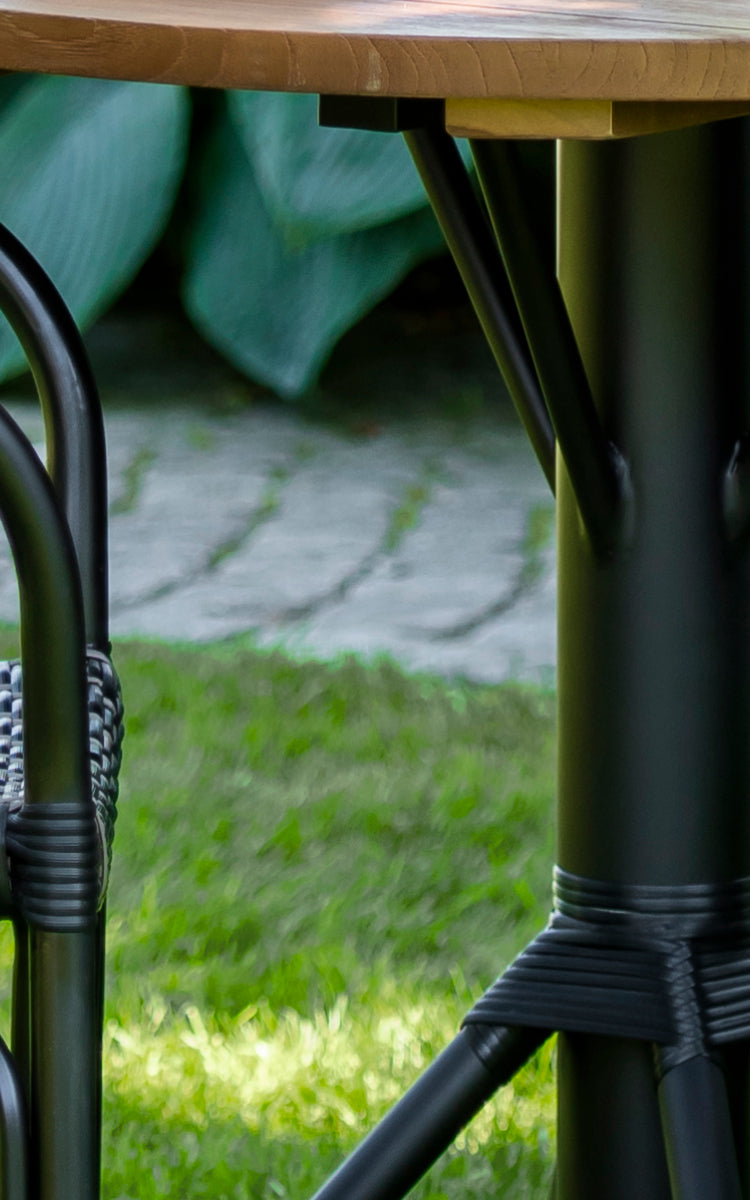 Dette er et nærbillede af Nicole Cafe Table i black aluminium frame black ArtFibre. Detalje af teaktoppen og den omviklede fod.