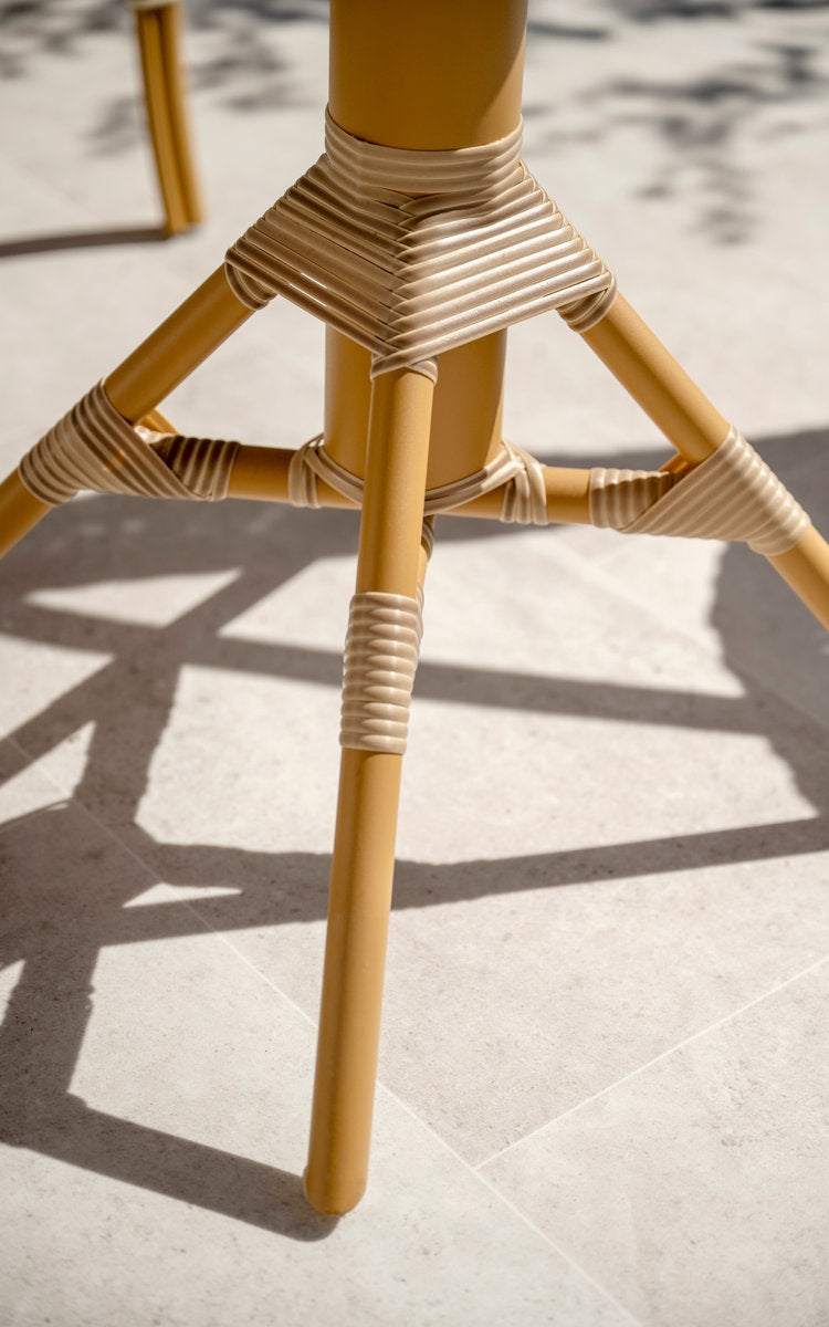 Dette er et nærbillede af Nicole Cafébord i almond aluminium frame natural artfibre. Stel med omviklede samlinger på en solrig terrasse.
