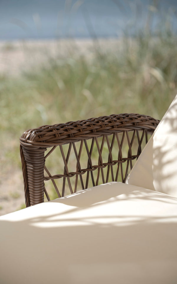 Dette er et nærbillede af Daisy Udendørs liggestol i brown artfibre aluminum. Flettet armlæn med cremefarvet pude.