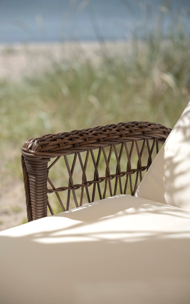 Dette er et nærbillede af Daisy Udendørs liggestol i brown artfibre aluminum. Flettet armlæn med cremefarvet pude.