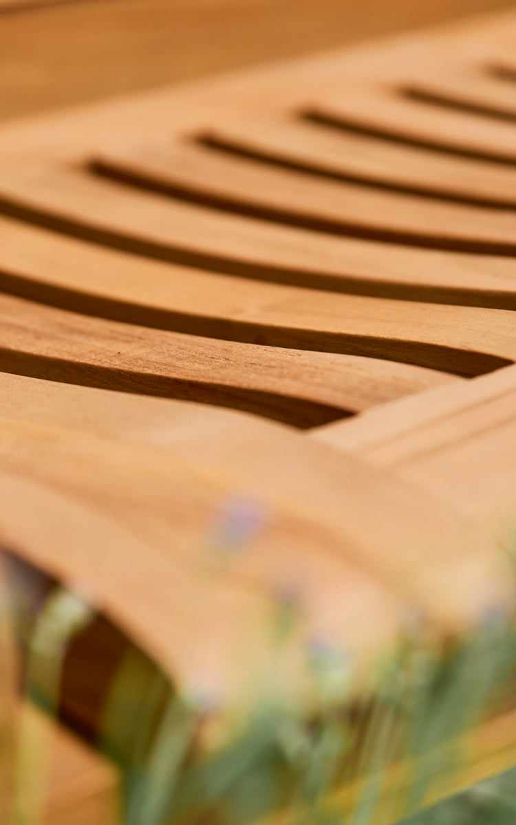 Dette er et nærbillede af St Catherine Teakbænk i teak outdoor. Detalje af de buede teaklameller på bænkens sædeflade.