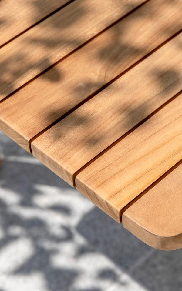 Dette er et nærbillede af Tobias Exterior Teak Table 205x91 cm i teak outdoor. Detalje af teakplankebordpladekanten og plettet sollys.
