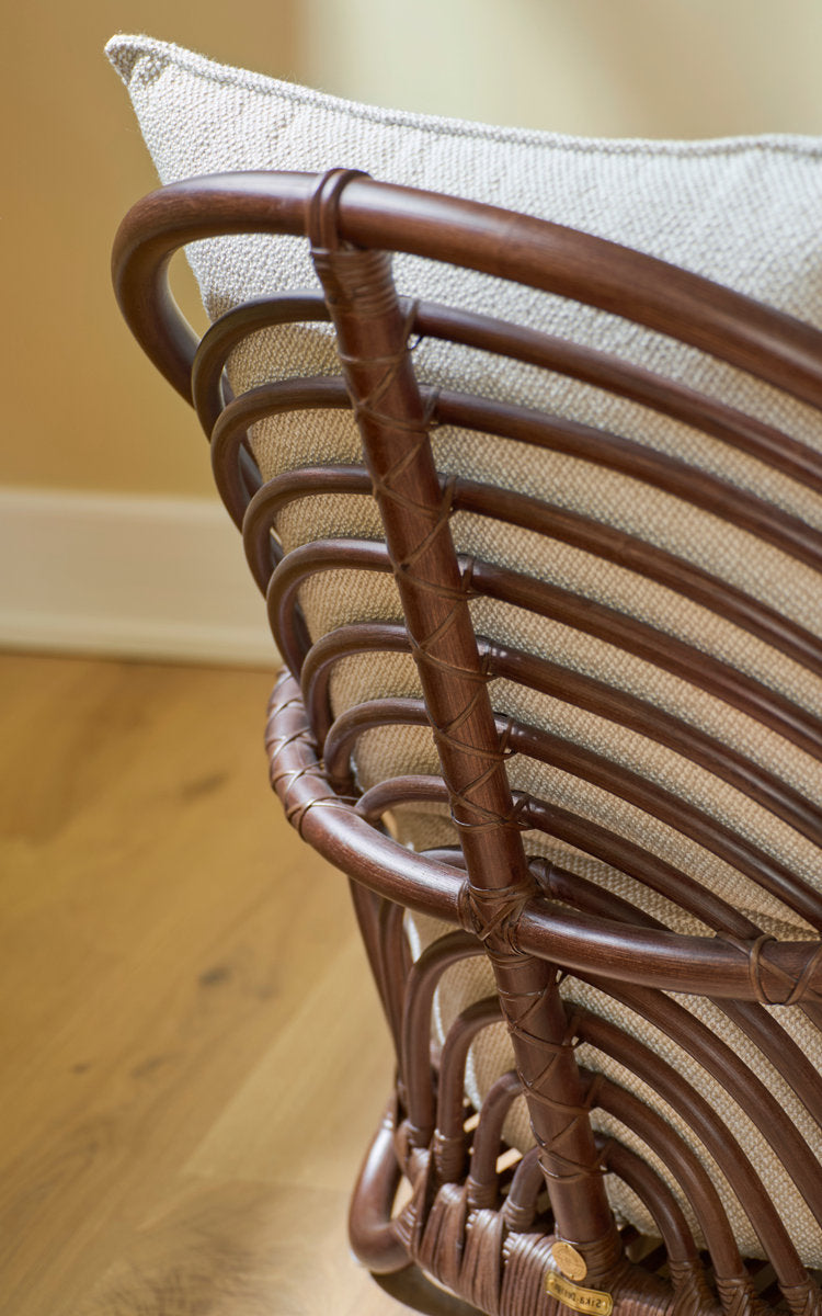 Dette er et nærbillede af Charlottenborg Lænestol i brown rattan. Buet rattanryg med linnedpude.