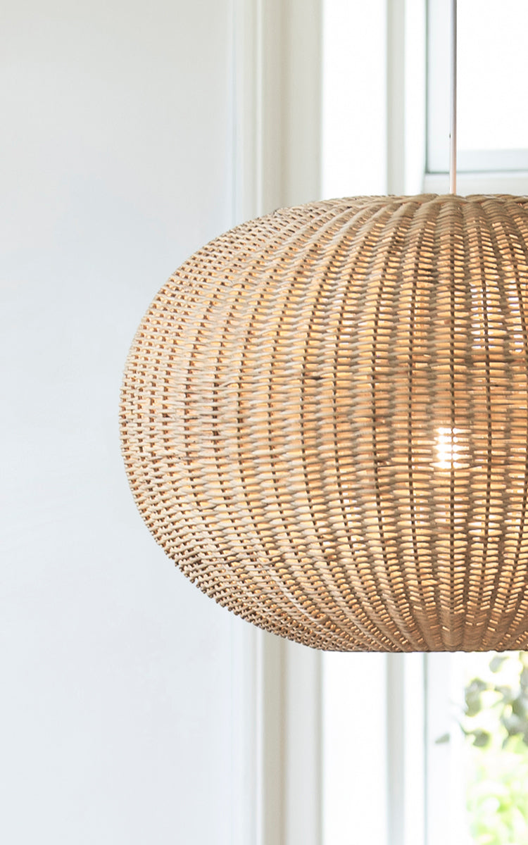 Dette er et nærbillede af Tangelo Lampshade Ø62 cm | Large i natural rattan. Detalje af den store rattanflet på den afrundede pendel ved et vindue.