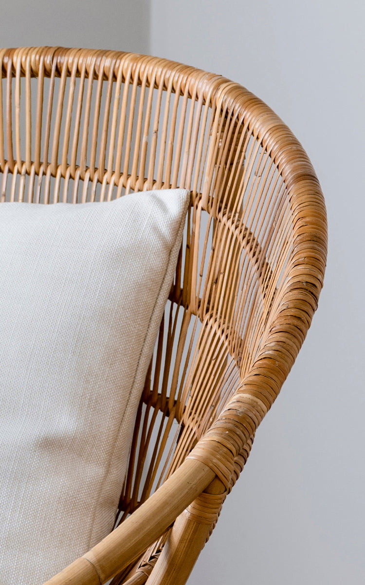 Dette er et nærbillede af Luna Lænestol i natural skin on rattan. Det buede stel med lodrette lameller og hvid pude fremhæver designet.