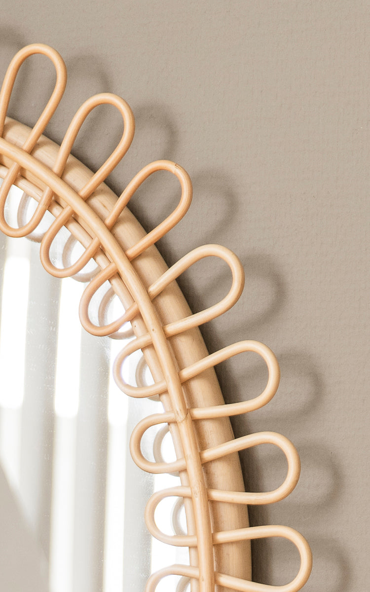 Dette er et nærbillede af Luella Spejl i polished natural rattan. Den dekorative løkkeformede rattanramme kaster elegante skygger på væggen.