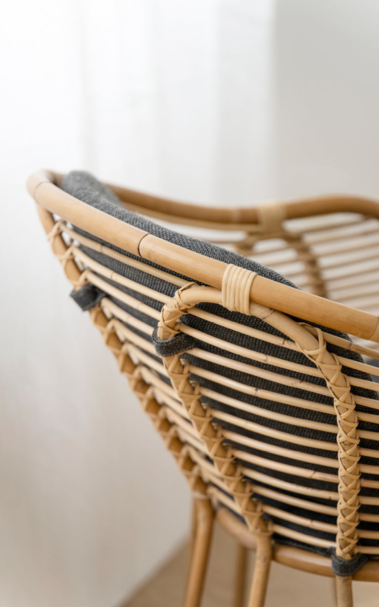 Dette er et nærbillede af Swing Lænestol i polished natural rattan. Detalje af den buede rattan-topskinne og flettede ryglænsbinding.