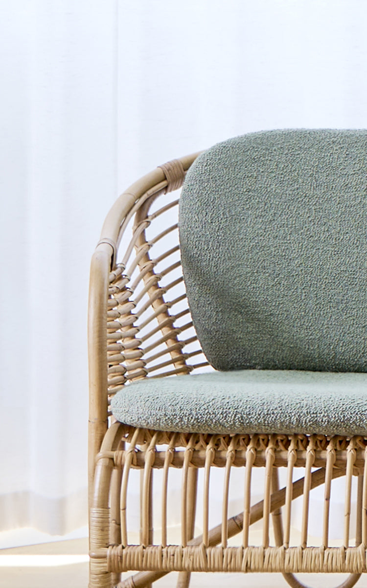 Dette er et nærbillede af Swing Sofa i polished natural rattan. Detalje af det buede rattan-sofastel med bouclé-sædehynde.