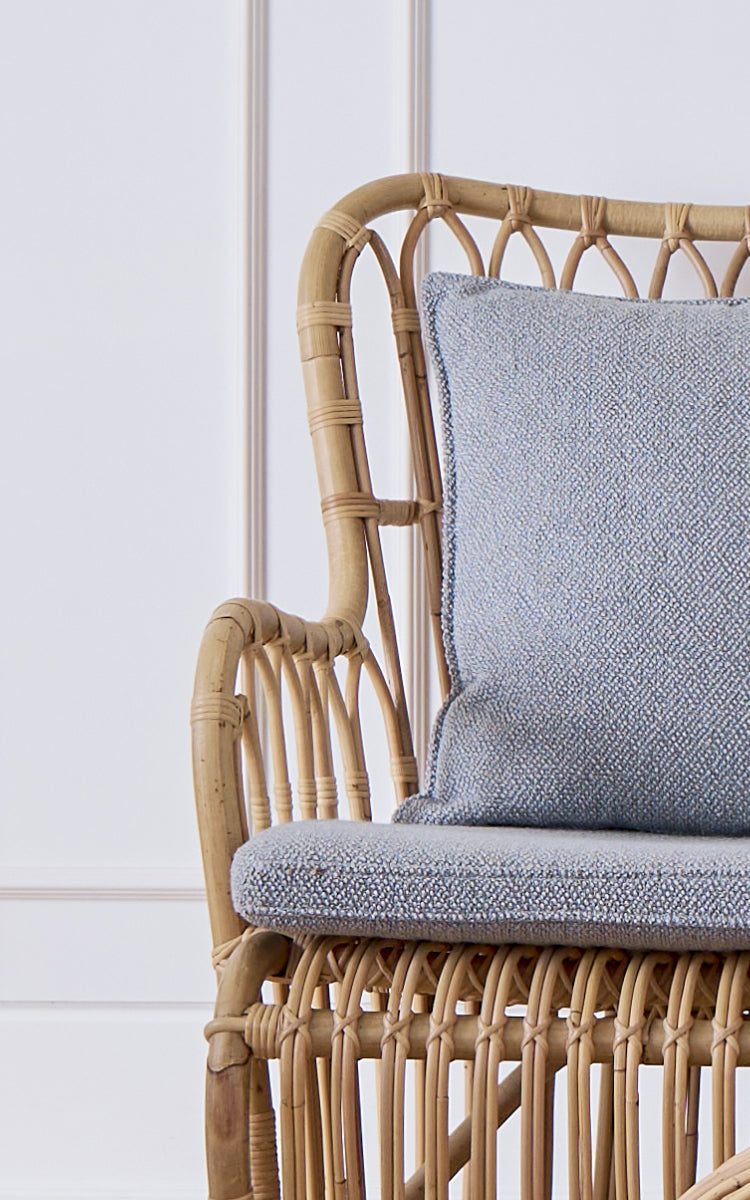 Dette er et nærbillede af Tulip Sofa i polished natural rattan. Detalje af rattan-sofastellet med buede stivere og bouclé-hynde.