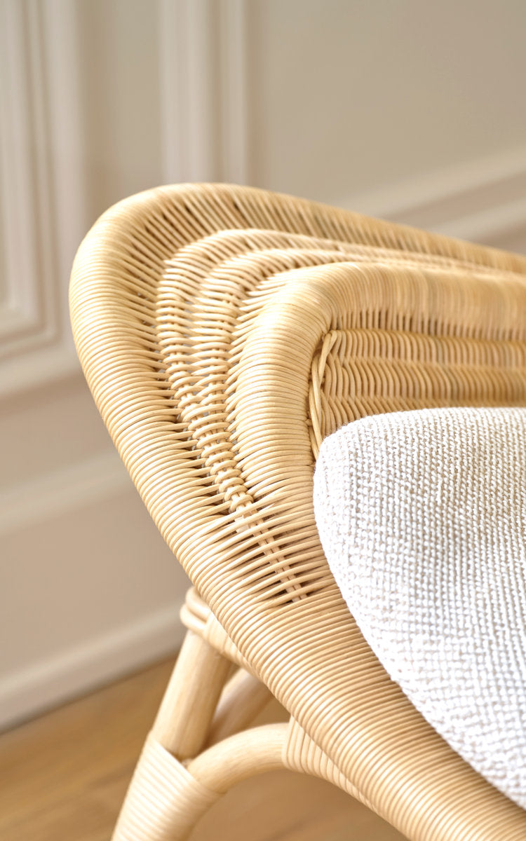 Dette er et nærbillede af Pacifique Lænestol i natural core weave rattan frame. Flettet skal med hvid pude ved en panelvæg.