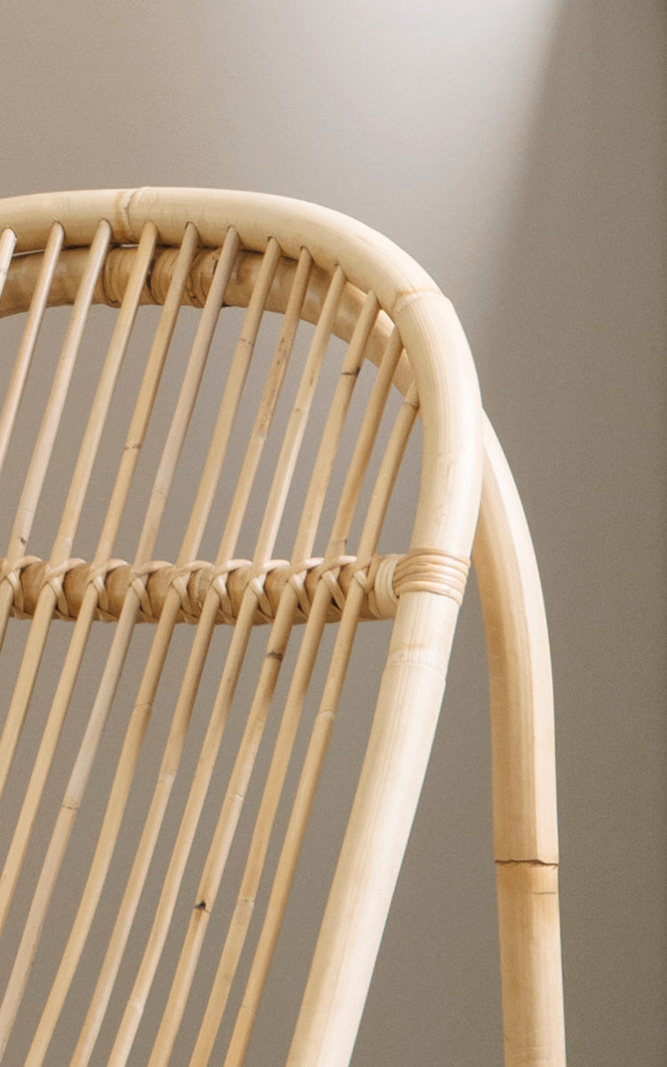 Dette er et nærbillede af Nanny Rocking Chair i polished natural rattan. Detalje af de glatte buede stænger og den cirkulære gyngebund.