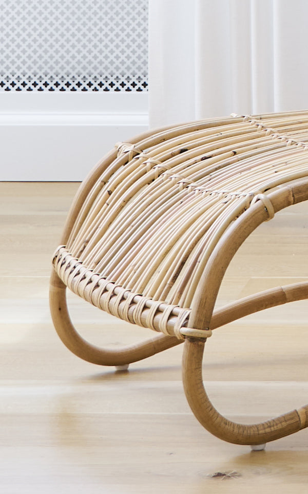 Dette er et nærbillede af Teddy Fodskammel i polished natural rattan. Detalje af de buede rattanskinner og flettede omvikling på fodskammel.