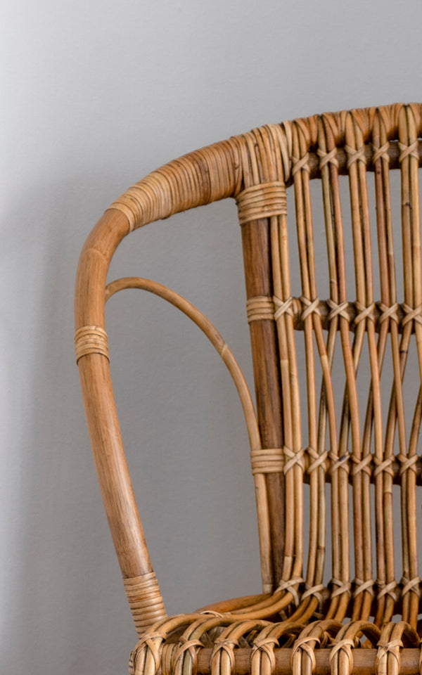 Dette er et nærbillede af Robert Spisebordsstol i polished antique rattan. Detalje af den buede rattan-arm og spindelryg med omviklede samlinger.