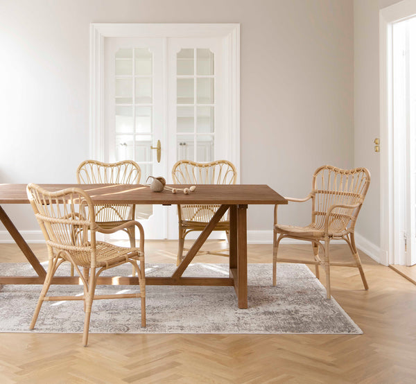 Dette er et livsstilsbillede af Margret Spisebordsstol i natural rattan. Placeret omkring et teakspisebord i et lyst skandinavisk rum med egegulv.