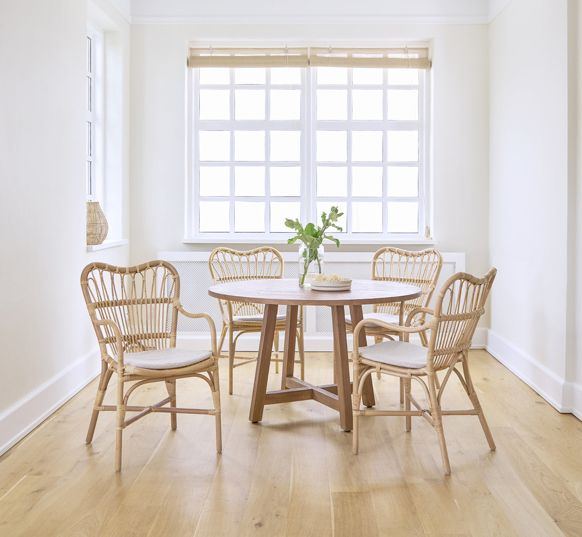 Dette er et livsstilsbillede af Margret Spisebordsstol i natural rattan. Lyst hvidt rum med rundt spisebord og egegulv.