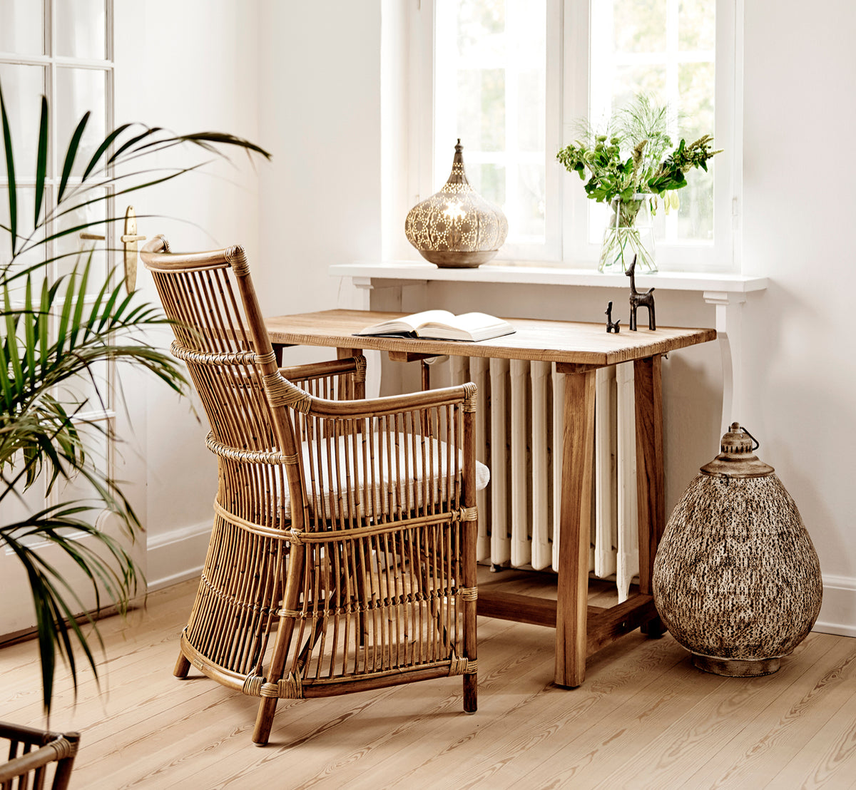 Dette er et livsstilsbillede af Davinci Spisebordsstol i antique rattan, i et lyst interiør med hvide panelvægge og sildebensgulv.