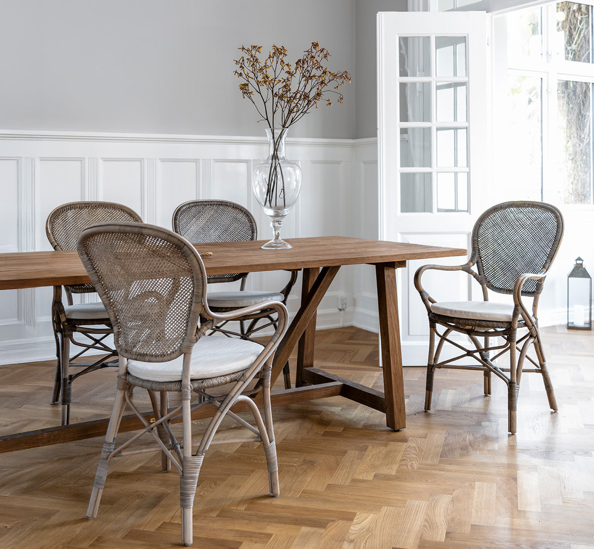 Dette er et livsstilsbillede af Rossini Spisestuelænestol i taupe rattan. Rundt om et spisebord af træ på et sildebensparketgulv.