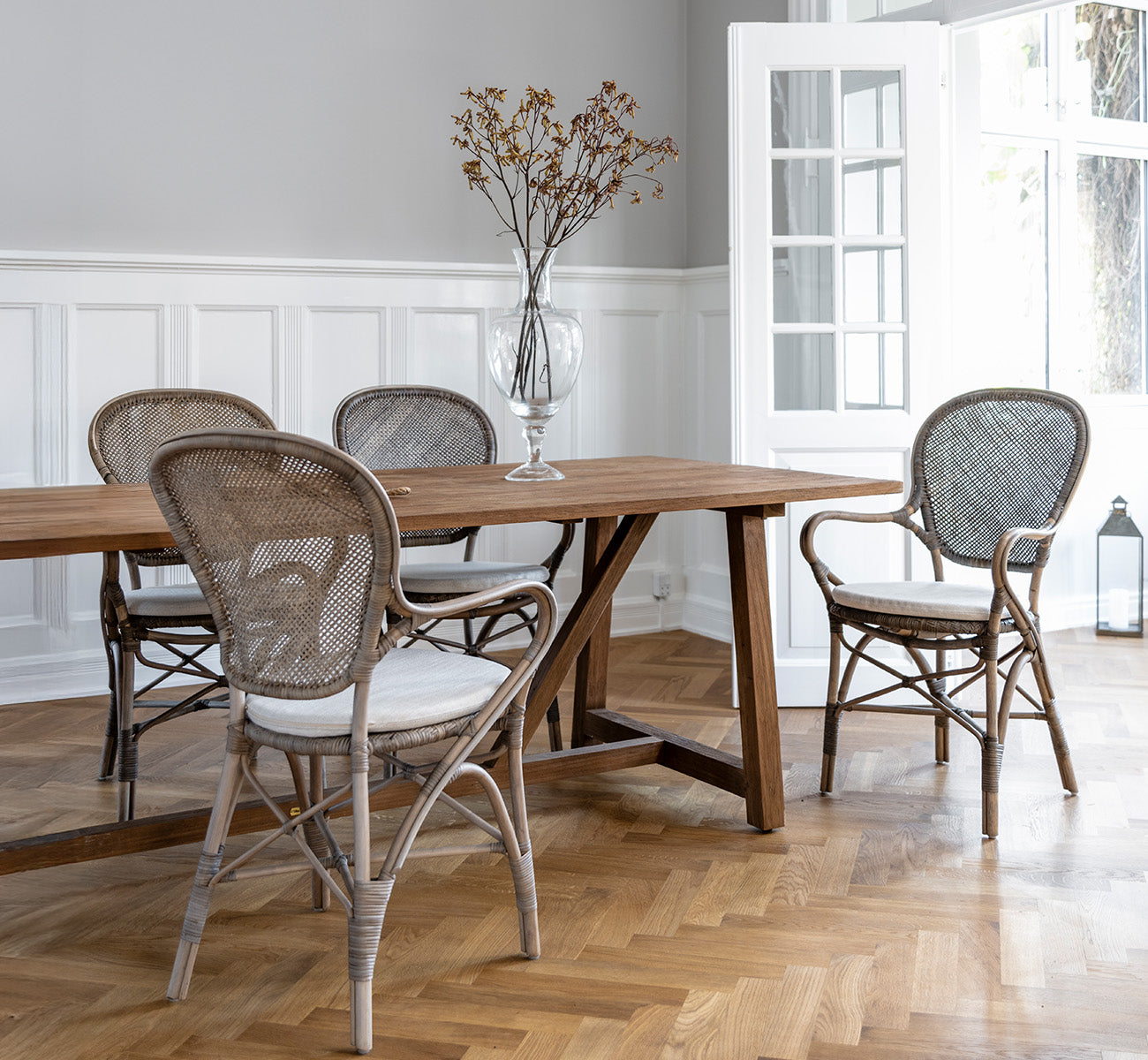 Dette er et livsstilsbillede af Rossini Spisestuelænestol i taupe rattan. Rundt om et spisebord af træ på et sildebensparketgulv.