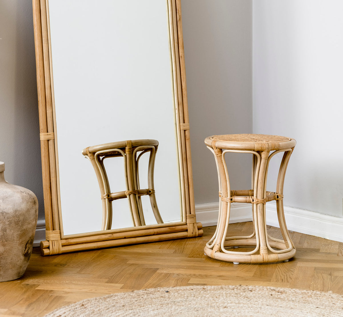 Dette er et livsstilsbillede af Bella Skammel i natural rattan, i et lyst interiør med hvide panelvægge og sildebensgulv.