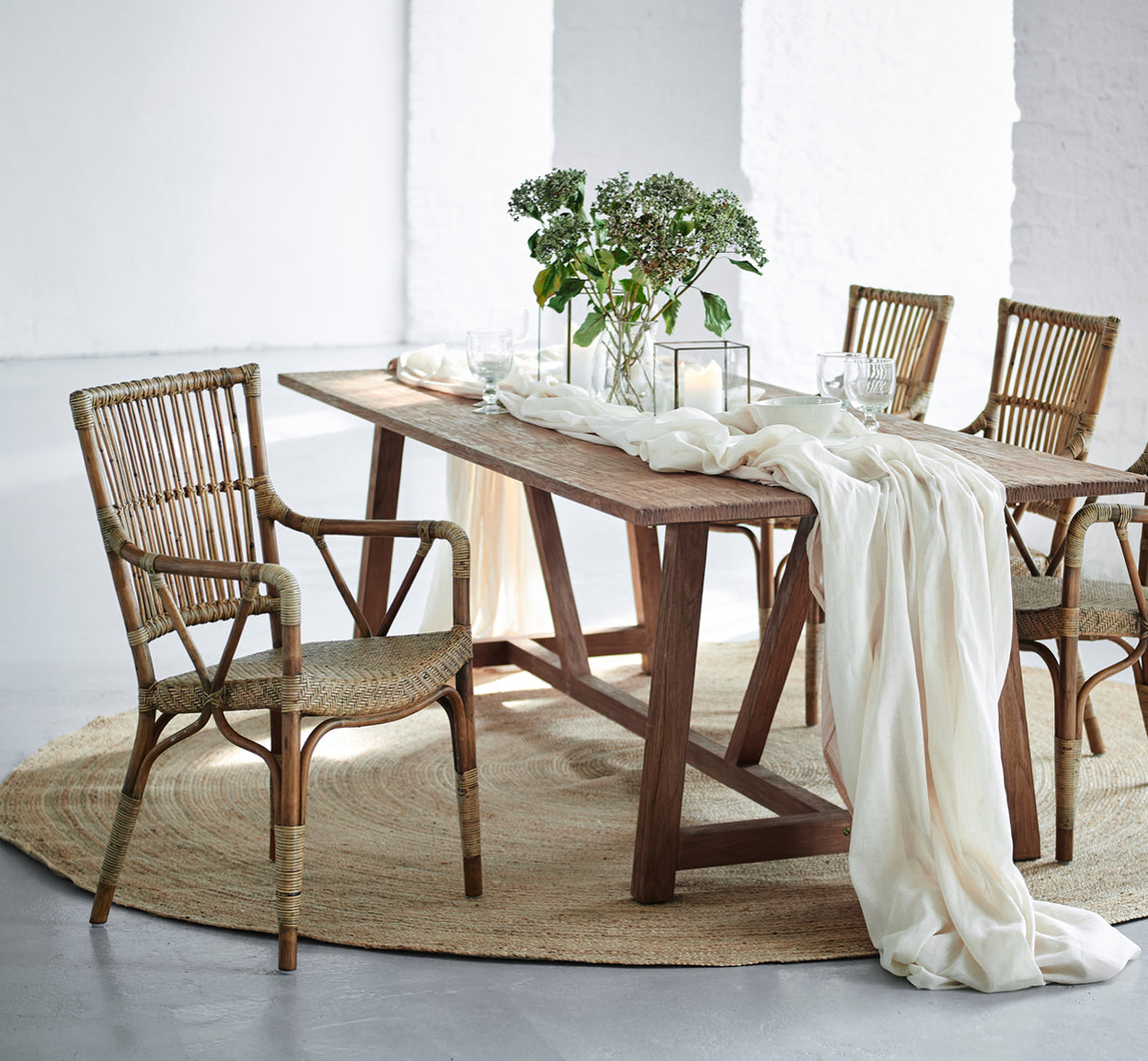 Dette er et livsstilsbillede af Piano Spisebordsstol i antique rattan. Rundt om et rustikt træbord med linnedløber og stearinlys.