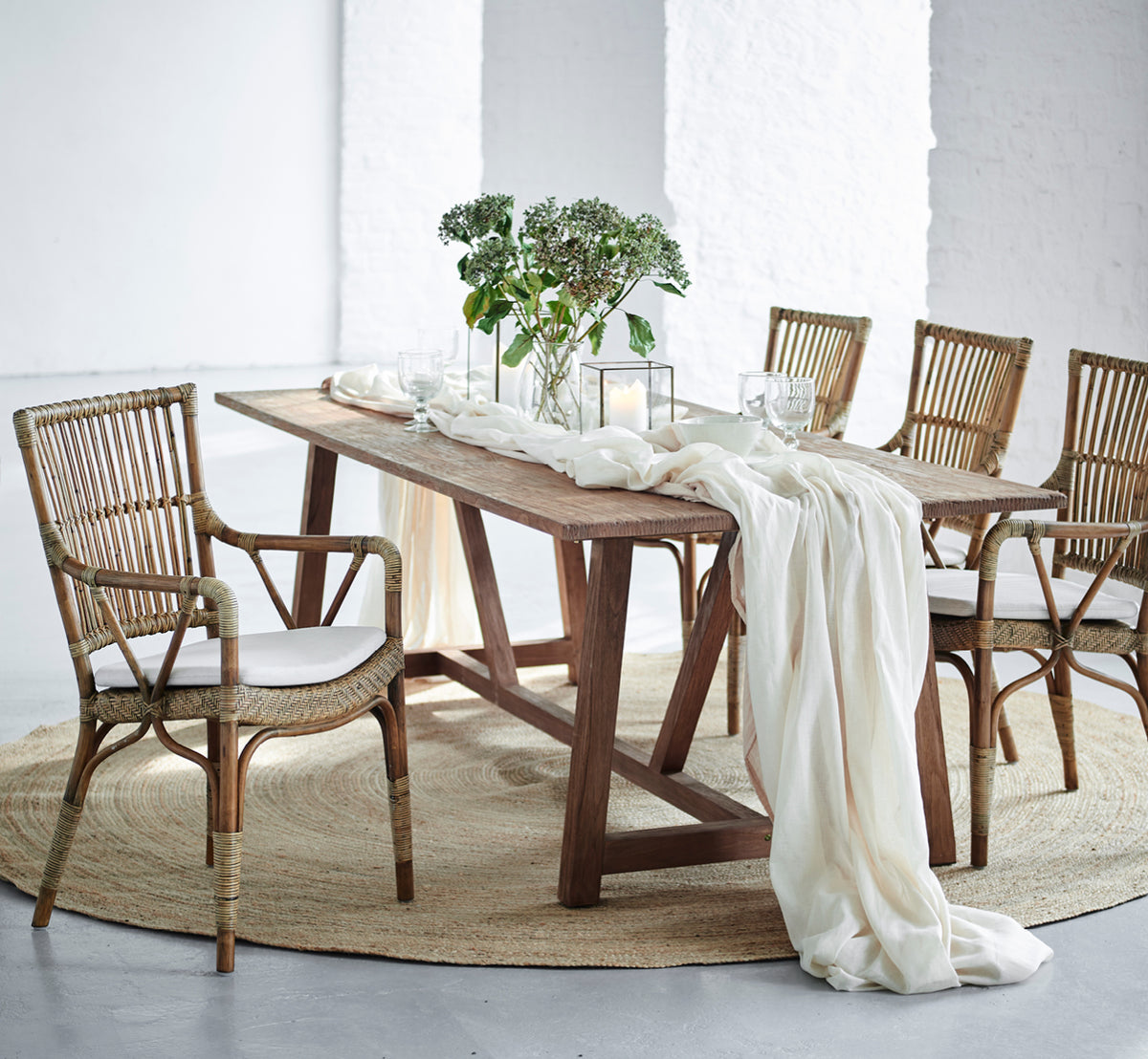Dette er et livsstilsbillede af Piano Spisebordsstol i antique rattan. Rundt om et rustikt træbord med linnedløber og stearinlys.