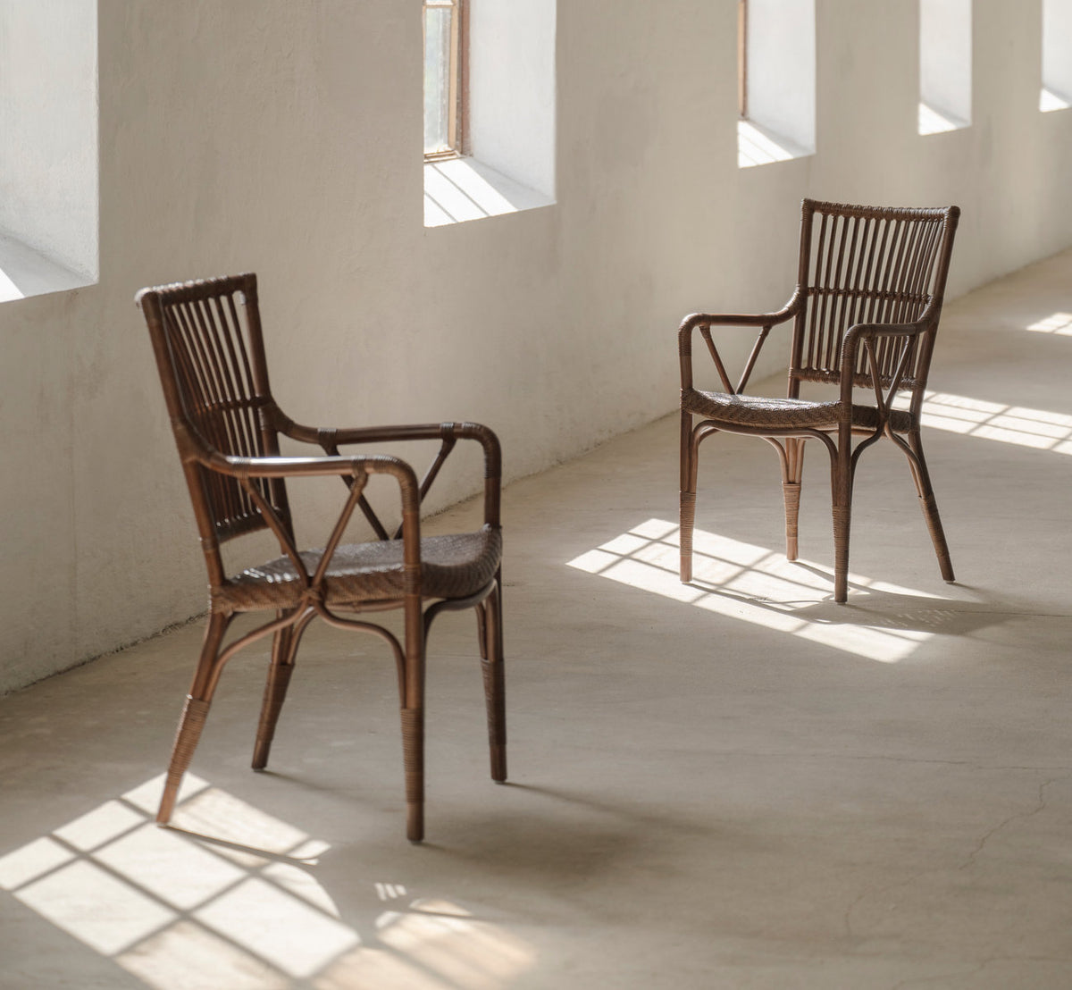 Dette er et livsstilsbillede af Piano Spisebordsstol i brown rattan. To i et solbeskinnet rum med betongulv.