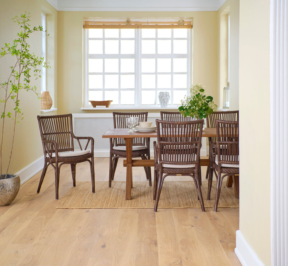 Dette er et livsstilsbillede af Piano Spisebordsstol i brown rattan. Omkring et teak spisebord ved et vindue.