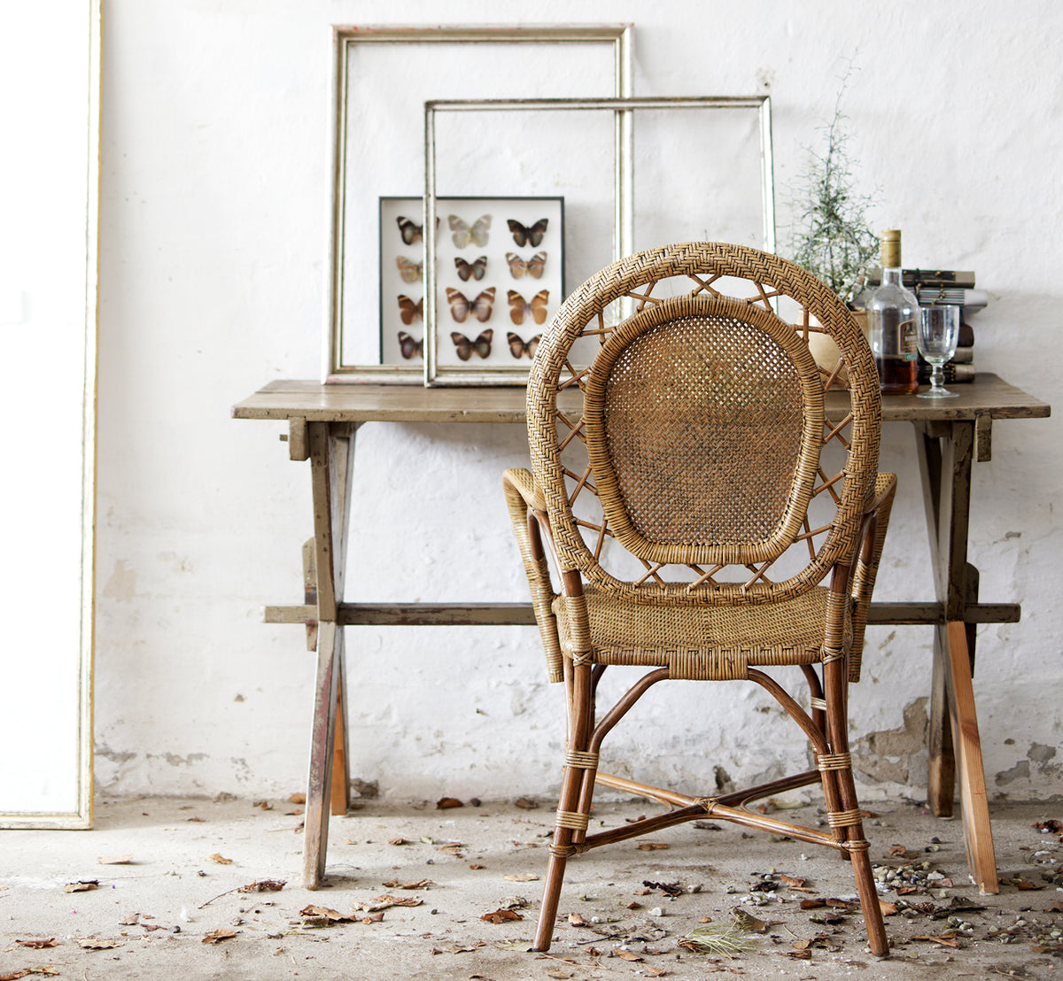 Dette er et livsstilsbillede af Romantica Spisebordsstol i antique rattan. Stylet ved et rustikt træbord med indrammet kunst i et vintage-miljø.