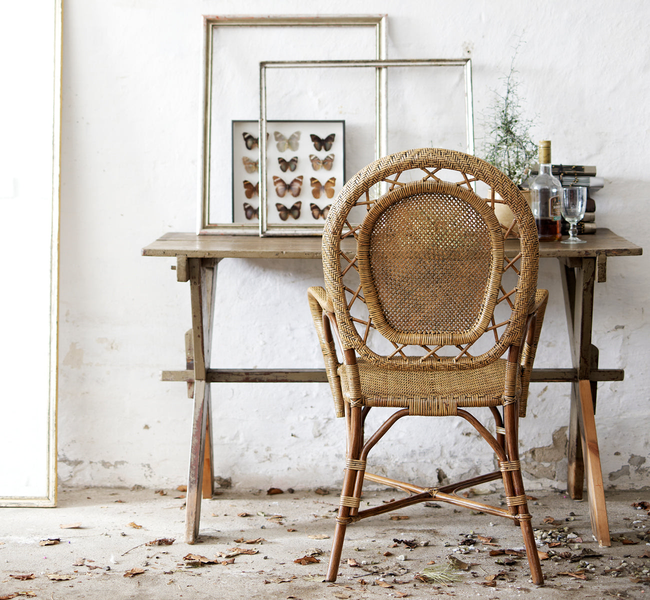 Dette er et livsstilsbillede af Romantica Spisebordsstol i antique rattan. Stylet ved et rustikt træbord med indrammet kunst i et vintage-miljø.